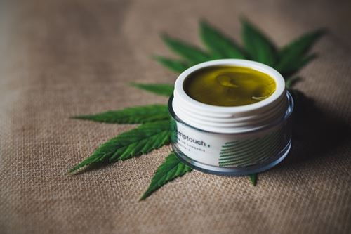 A pot of CBD cream next to a hemp leaf